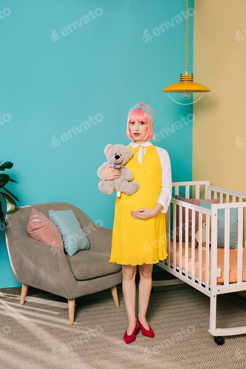 Preview: retro styled pregnant pin up woman with pink hair standing with teddy bear in child room