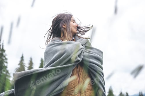 Preview: A young woman wrapped in a blanket in the mountains.