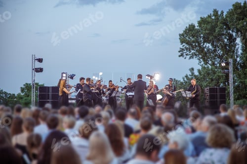 Preview: Orchestra performing live concert for audience under blue sky