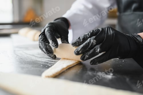 Preview: Baker rolling dough for croissants in bakery kitchen