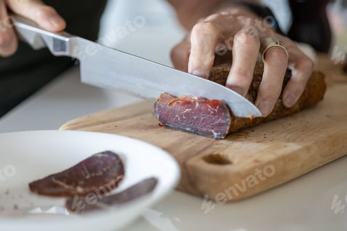 Preview: Chef preparing a meal in a kitchen, slicing pieces of pastirma on a wooden cutting board