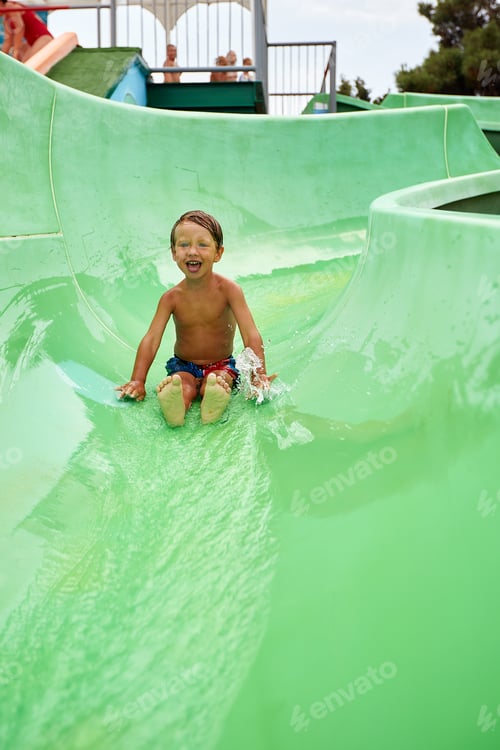 Preview: A little boy slides down a green water slide in the water park, a child's cheerful mood, holidays