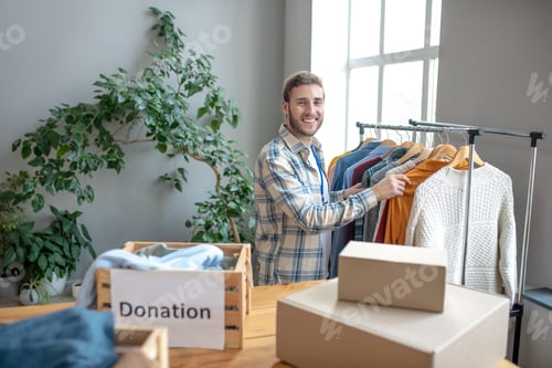 Preview: Young man standing at a rack with clothes.