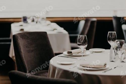 Preview: Cutlery and wine glasses on white tablecloth, empty armchairs near