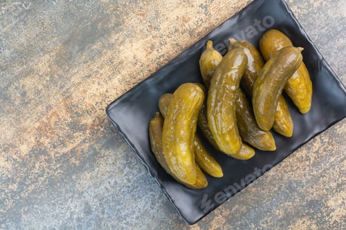 Preview: A dark plate full of delicious pickled cucumbers on white background