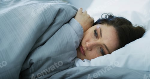 Preview: Sad, woman and relax on bed at house with depression, mental health problem and insomnia anxiety. G