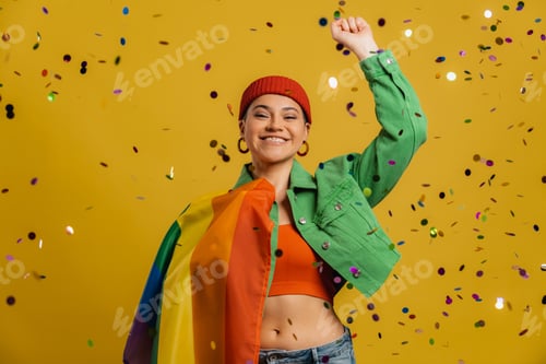 Preview: Happy woman carrying rainbow flag and gesturing while confetti flying against yellow background