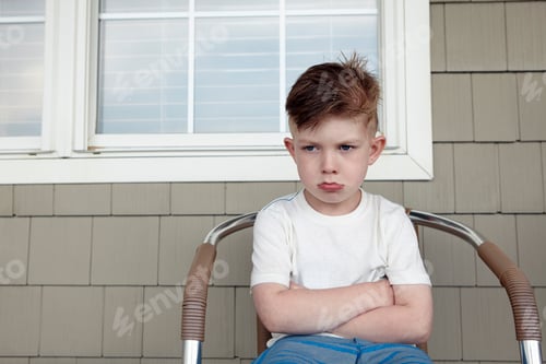 Preview: Portrait of boy sitting outside house sulking