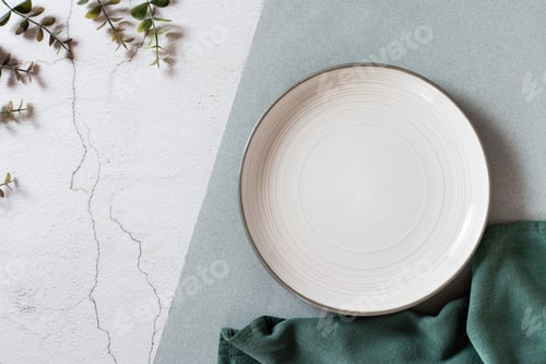 Preview: Empty ceramic plate, eucalyptus branches and fabric on a two-tone background. Eco concept. Top view