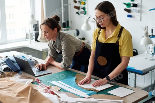 Preview: Mature female tailor putting pattern on piece of leather against colleague