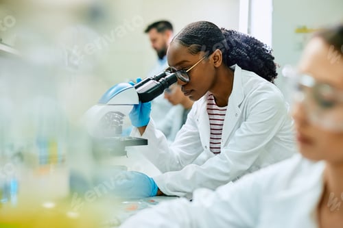Preview: Black female scientist looking through microscope while working in laboratory.