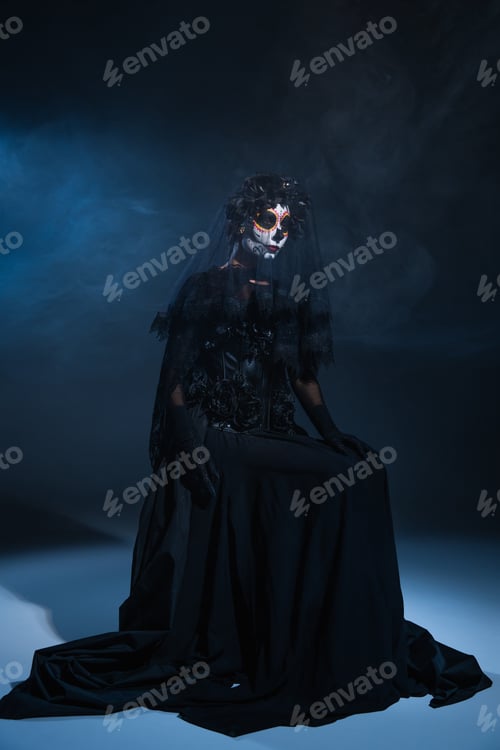 Preview: woman in halloween makeup and black witch dress sitting on dark smoky background with blue light