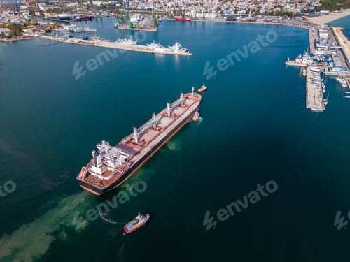 Preview: A massive cargo ship bulk carrier leaves the seaport, accompanied by tugboats, aerial view