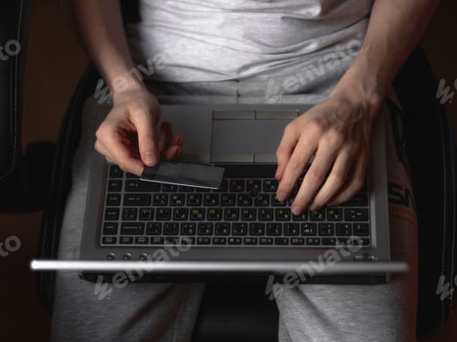 Preview: The hands of a young caucasian man holds a bank card with one hand, and with the other he types