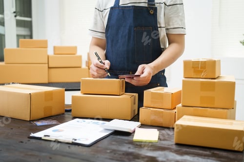Preview: A man is working at his desk, preparing parcel boxes for shipment. He checks packs items carefully