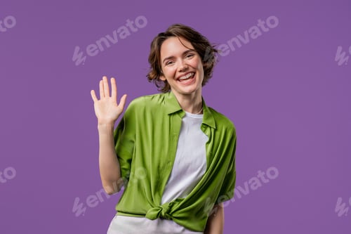 Preview: Friendly young adult woman waving hand - Hello, Hi. Greetings, Salute on violet.