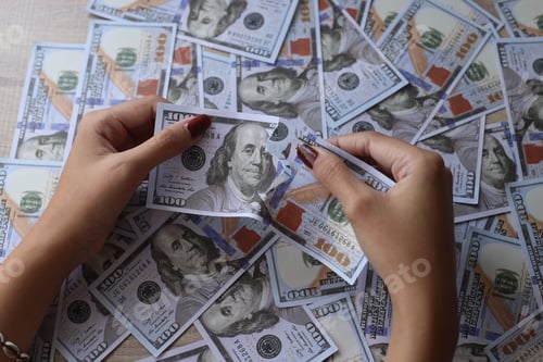 Preview: Close-up hands holding torn money on dollar bills background.