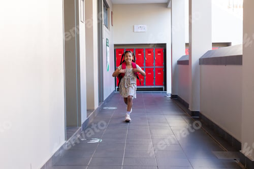 Preview: Happy biracial schoolgirl walking with school bag in corridor at elementary school, copy space