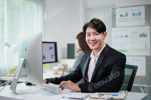 Preview: Asian businessman smiling and working on computer in office