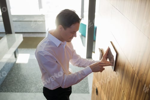 Preview: man controls smart home devices using digital tablet with launched application on background of room