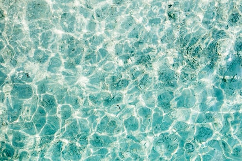 Preview: Clear turquoise water reflecting sunlight along a serene beach in the afternoon,