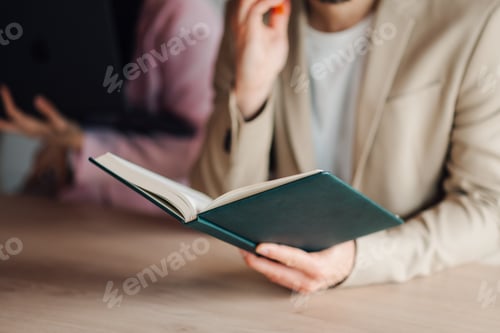 Preview: Businessman reading book and touching face in thoughtful pose