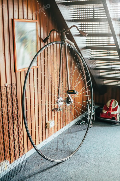 Preview: Old fashioned bicycle with one big and one small wheel under the stairs in a house. Selective focus