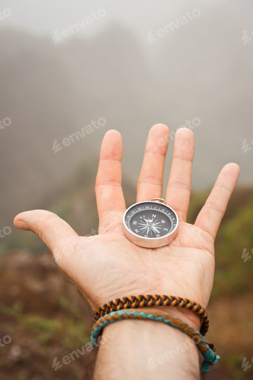 Preview: Hand with compass in the misty mountain terrain