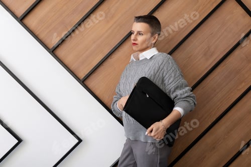 Preview: businesswoman with a short haircut with a leather folder for documents in her hands against the wall