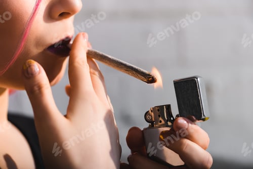 Preview: cropped view of girl lighting up and smoking joint with medical marijuana