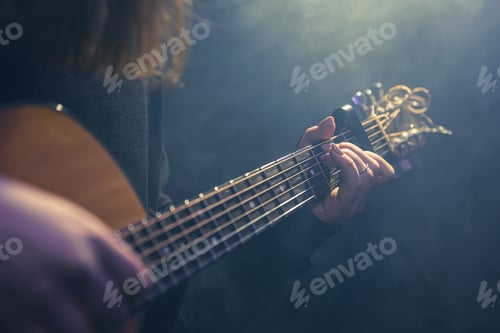 Preview: Young woman playing acoustic guitar in a dark room with haze.
