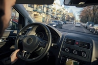 Preview: Steering wheel and hand of a man driving a car through the city