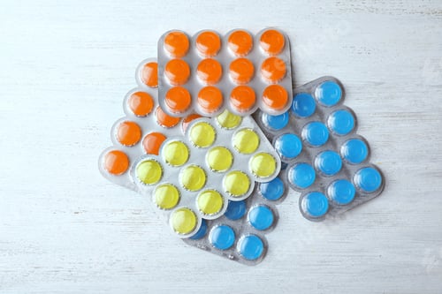 Preview: Blisters with color cough drops on white wooden table, top view