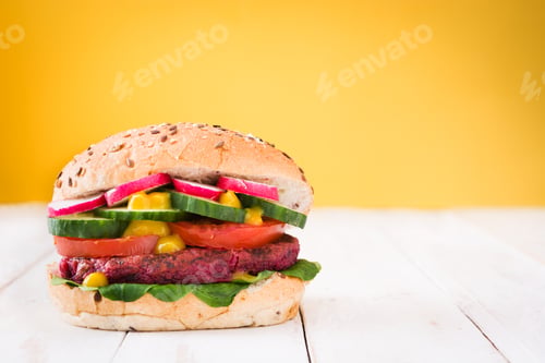 Preview: Delicious vegan beet burger showing fresh ingredients on white table and yellow background