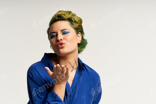 Preview: Vibrant young woman blowing kisses in stylish fashion shoot with elegant makeup and bold colors