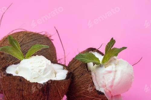 Preview: Vanilla ice cream balls in fresh coconut halves decorated with mint leaves on a pink background