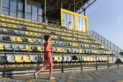 Preview: Young woman running during sunny morning on stadium