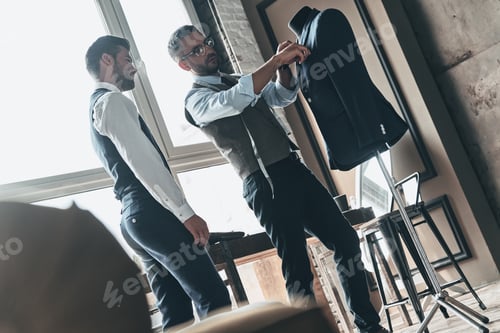 Preview: Working on trending designs. Two young fashionable men looking at jacket while standing in workshop