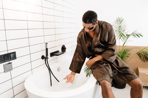 Preview: Black man dressed in robe using eye patches while sitting on bath