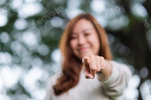 Preview: Blurred image of a beautiful young asian woman pointing finger to the camera in the park