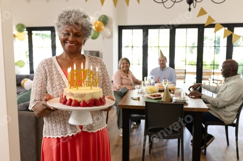 Preview: Elderly woman carrying birthday cake with candles, smiling at family gathering