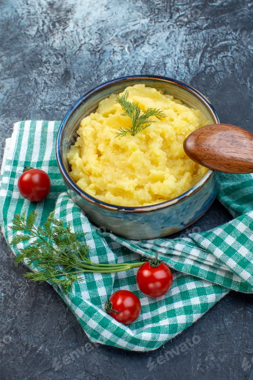 Preview: Close up view of mashed potatoes served with dill wooden spoon fresh tomatoes on green stripped