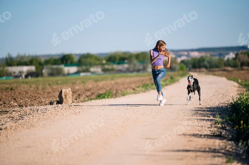 Preview: Beautiful young blonde woman running in the field with her greyhound dog.