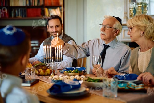 Preview: Jewish extended family lighting the menorah during Hanukkah meal at dining table.