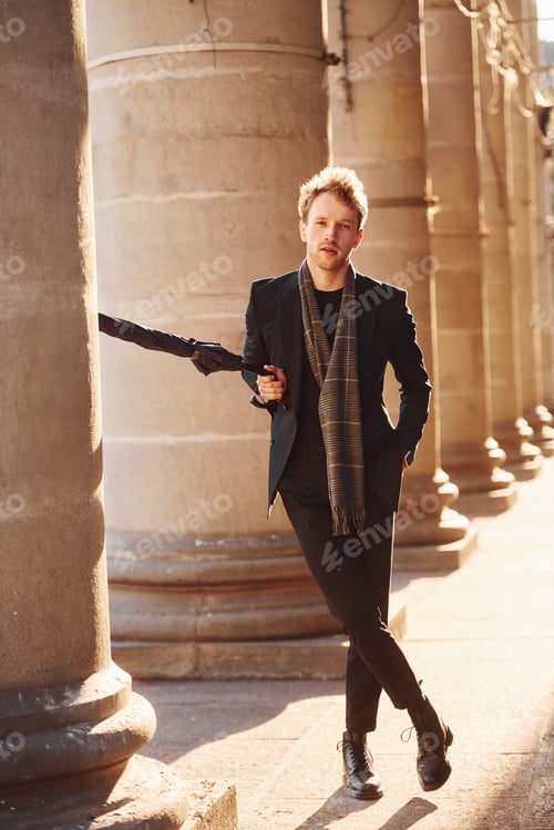 Preview: Holding umbrella. Elegant young man in formal classy clothes outdoors in the city