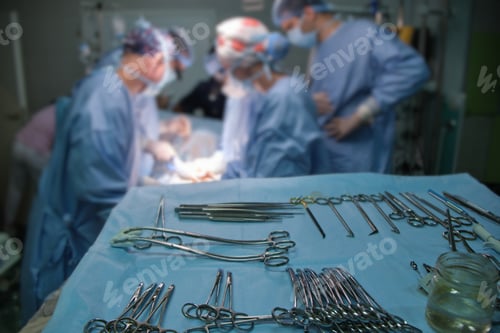 Preview: Closeup of surgical tools on table and team of surgery doctors operating a patient in hospital room