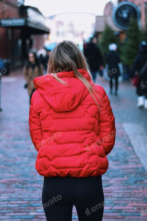 Preview: Young teenage girl in a red winter jacket is walking in an old town neighborhood on a cold day