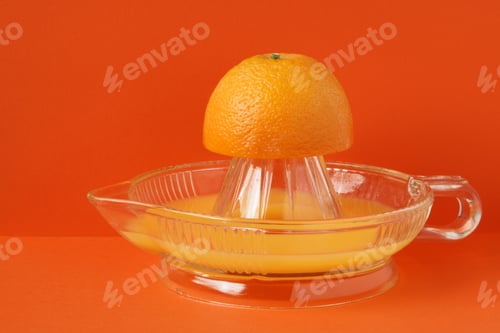 Preview: Bold orange two tone background with glass orange juice juicer with juice and orange half Copy space