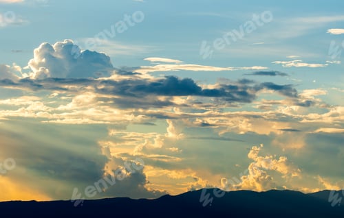 Preview: Golden Light Radiating Through Clouds Above Silhouetted Mountains