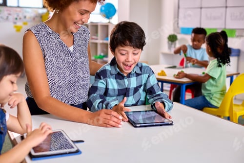 Preview: Female Teacher With Multi-Cultural Elementary School Pupils Using Digital Tablets At School